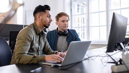 two men sitting at a table working on a laptop
